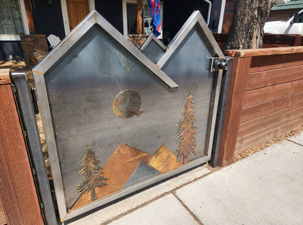 Steel yard gate with pine trees and mountain peaks